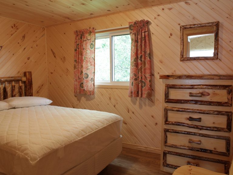 Interior of wood-panelled cabin, showing bed, window, and dresser