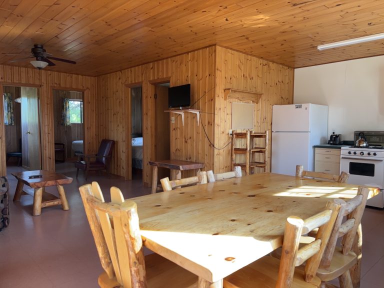 Interior of wood-panelled cottage, with kitchen table with seating for six prominent and kitchen in background