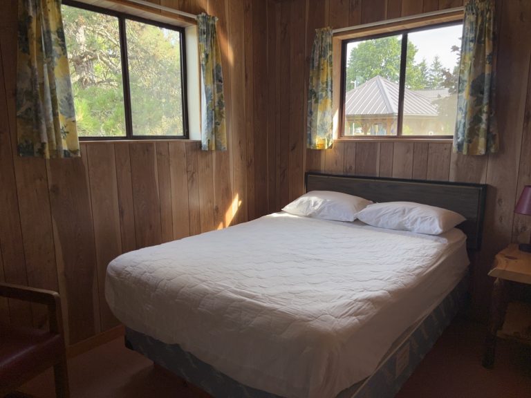 Interior of wood-panelled cottage bedroom, with two windows above and to the side of the bed