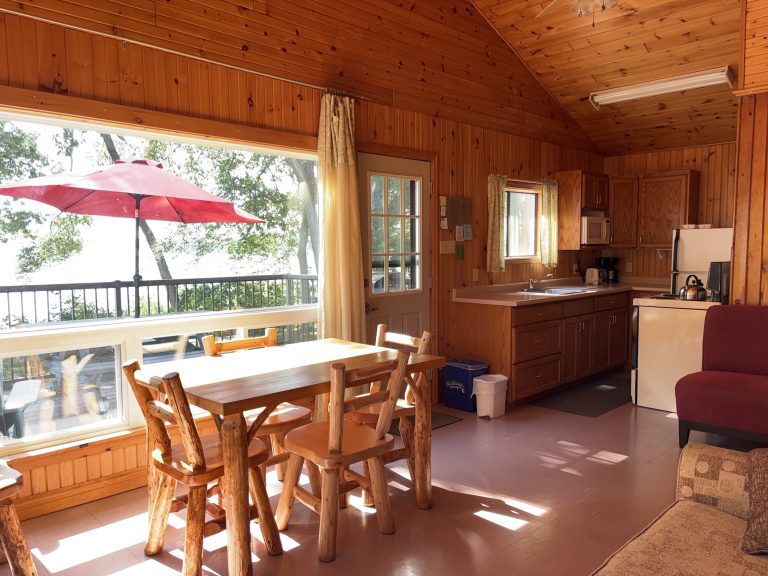 Sunny interior of a wood-panelled cottage, showing main window and dining table
