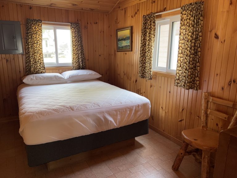 Interior of wood-panelled cottage, with two windows, chair, and bed