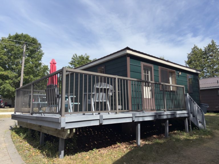 Exterior of green wooden cottage, with deck in the foreground