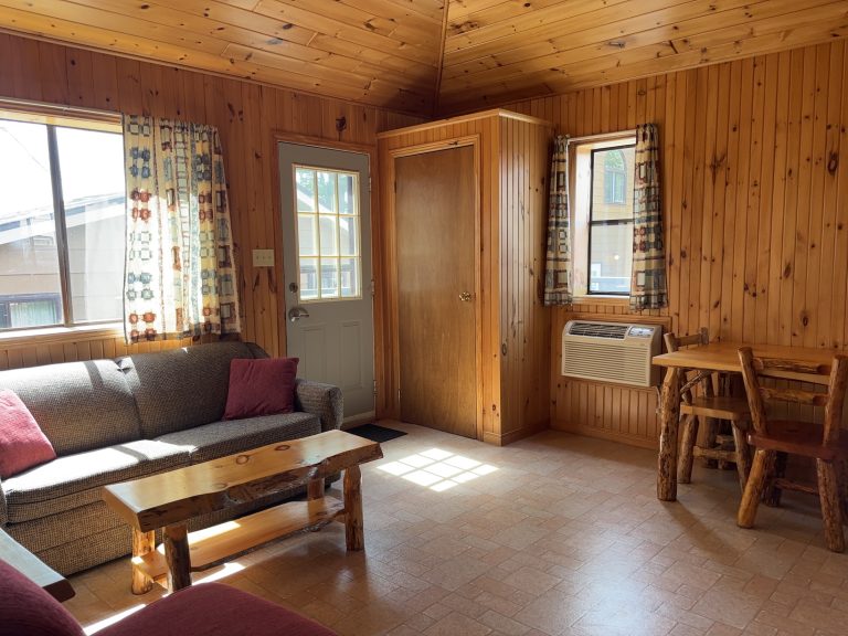 Interior of wood-panelled cottage, showing seating area, door, windows, and table