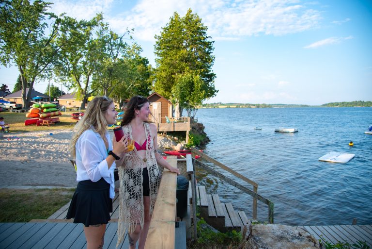 Two smiling women stand at a railing looking out across a blue lake