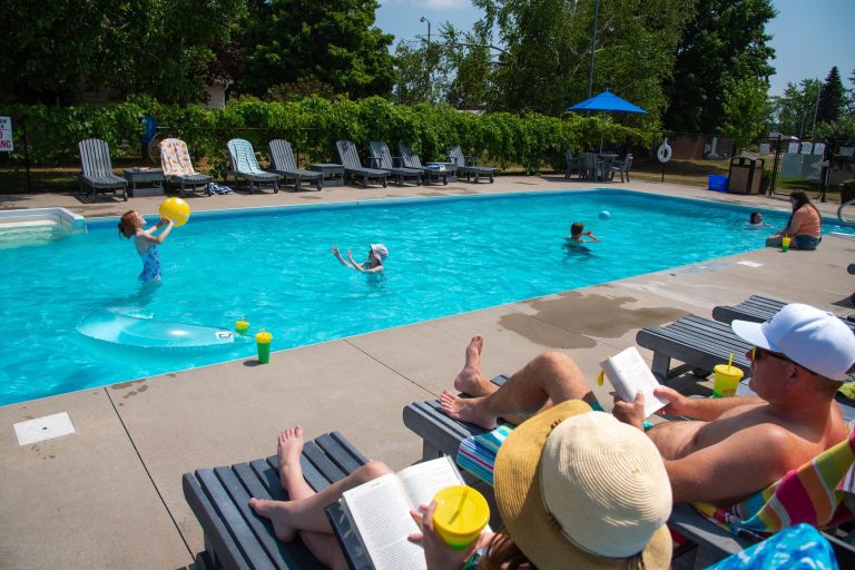 Two adults lounge by a pool while children play in the water
