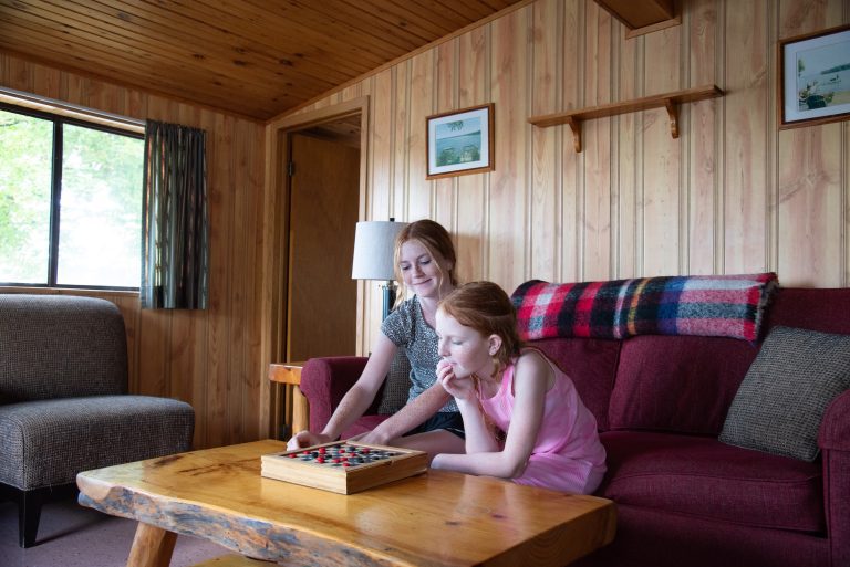 Two girls plays checkers in a wood-panelled cabin