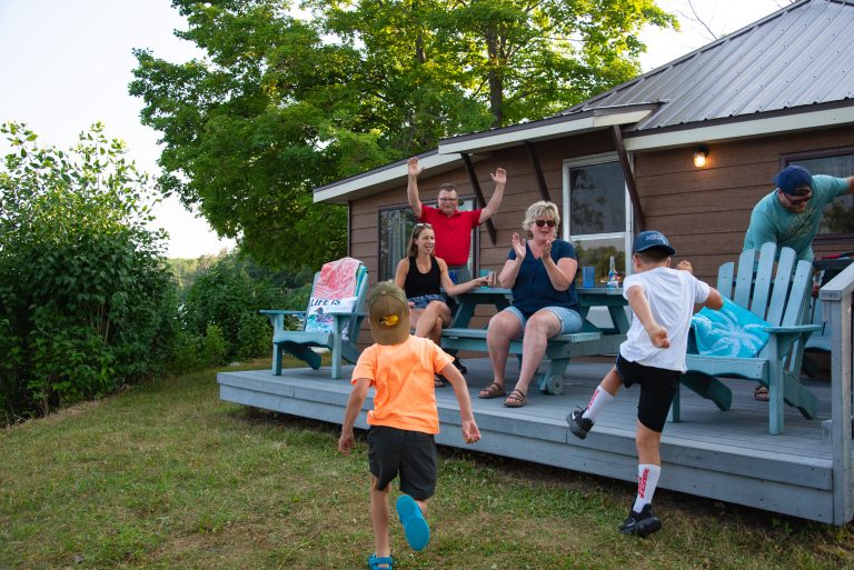 Children rush towards a cottage patio where adults are sitting