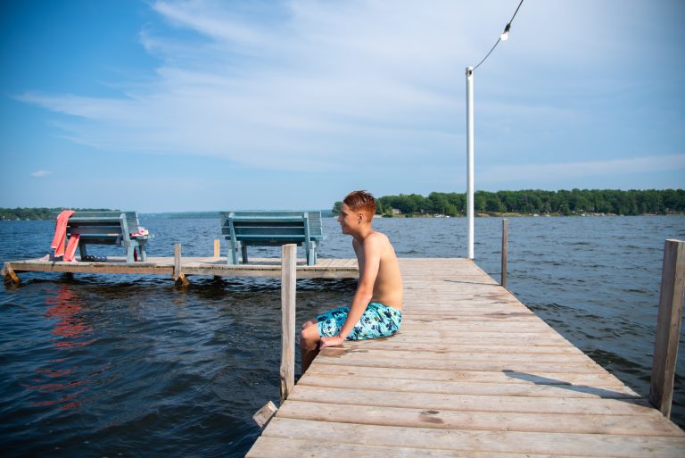 A young person sits on a dock looking out at the water