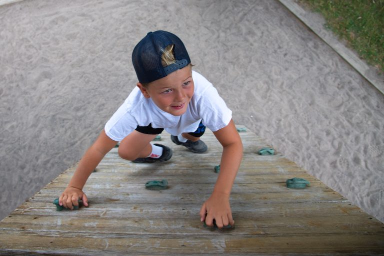 A child, looking up towards the camera, climbs a human-made rock wall