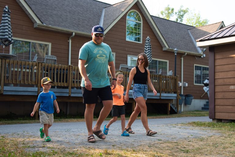 A family of four walks past the exterior of a brown cottage