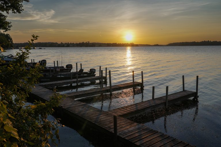 The sun sets across a lake, silhouetting a long dock